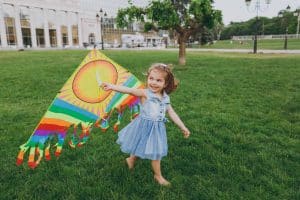 Joyful little cute child baby girl in denim dress walking, play with colorful kite and have fun in green park. Mother, little kid daughter. Mother's Day, love family, parenthood, childhood concept.